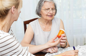 Woman handing an older woman a prescription bottle