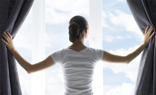 Woman looking out of an open window at a blue sky